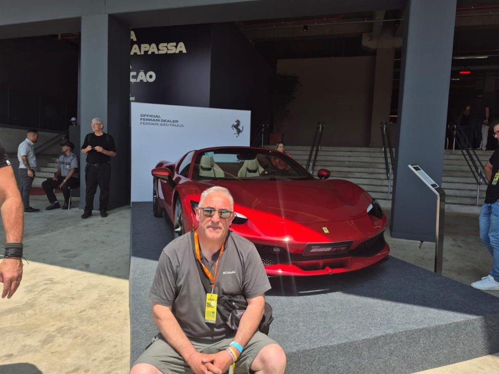 César sentado junto a un Ferrari rojo en exhibición en Interlagos